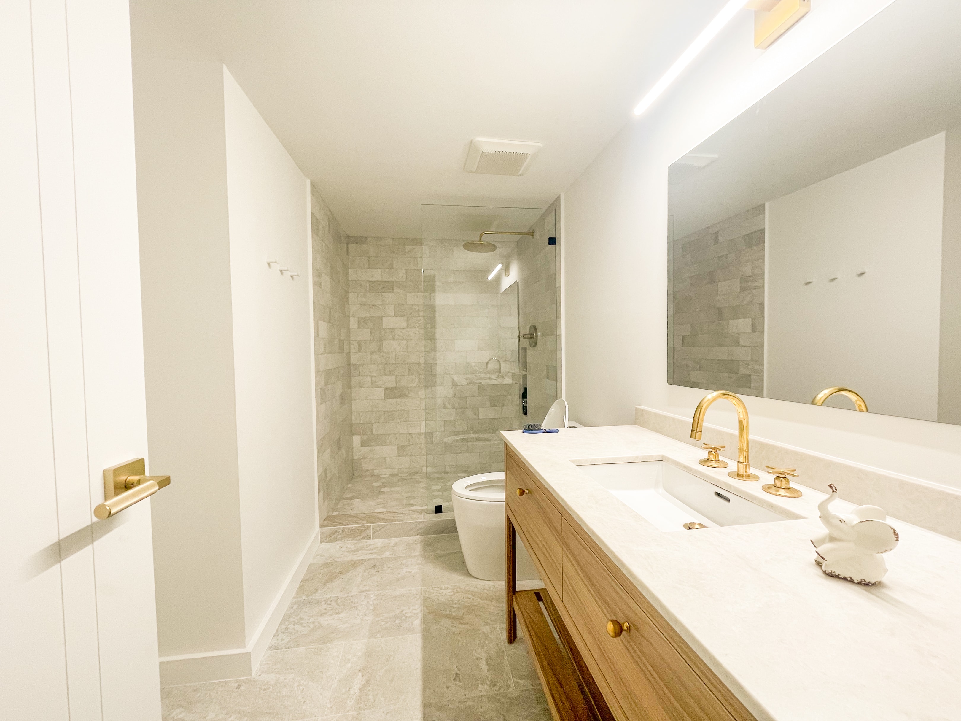 Full-length double vanity with marble countertop, brass fixtures, and glass shower