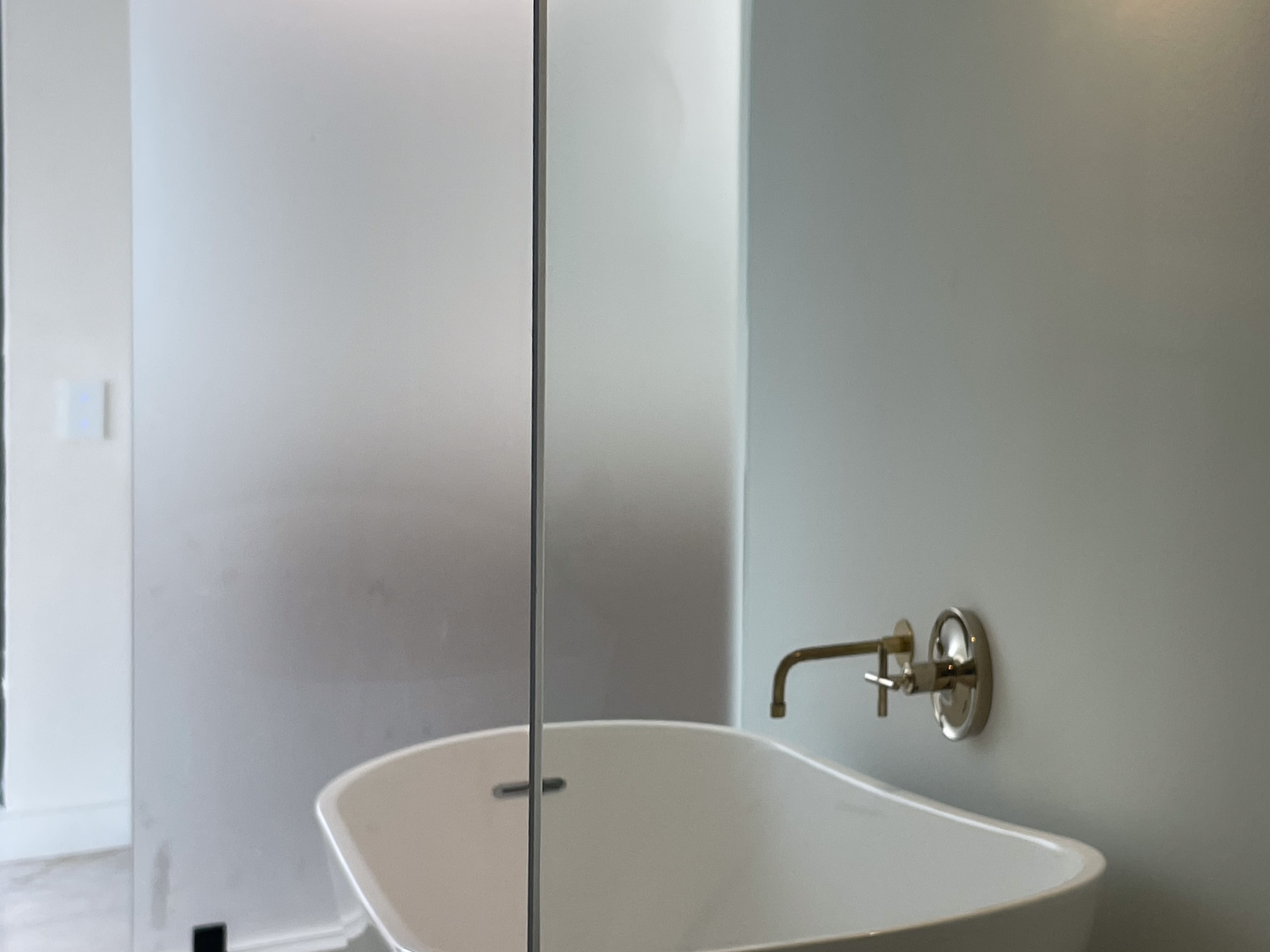 Freestanding soaking tub with wall-mount brass faucet and frosted glass partition