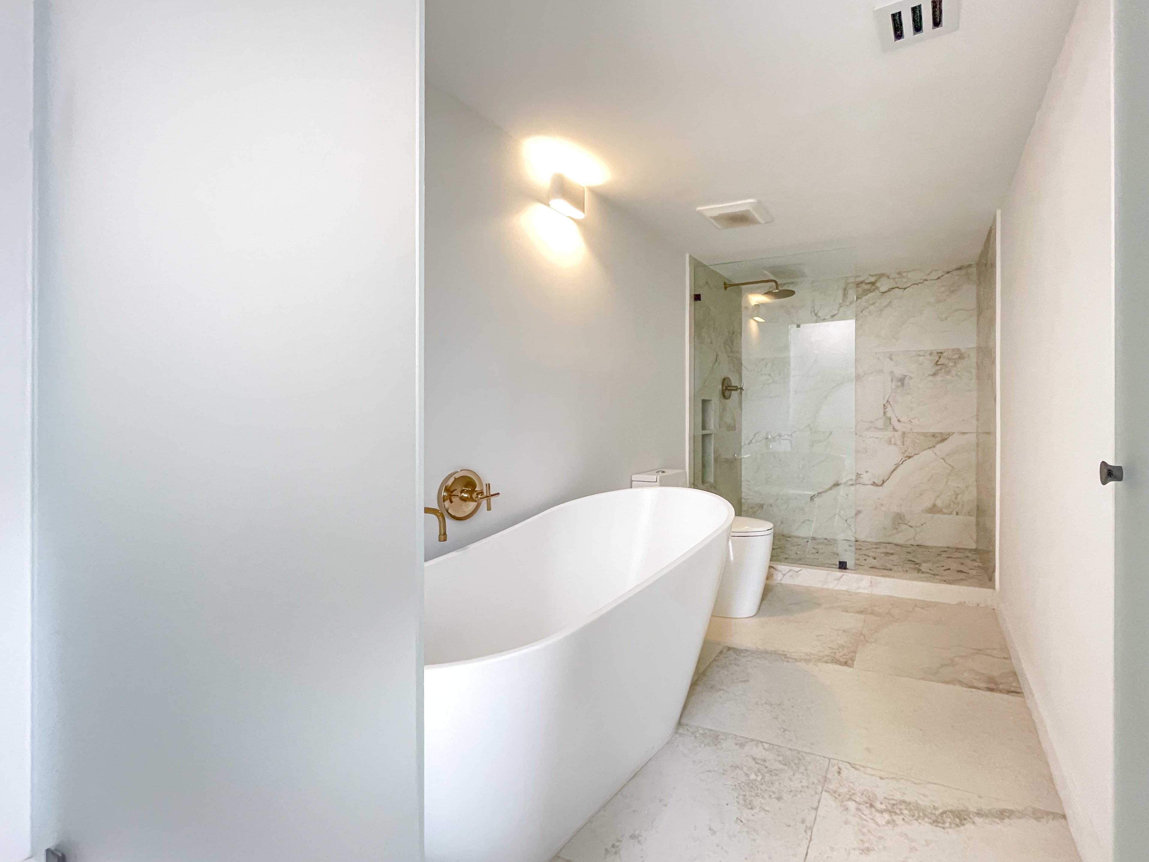 Primary en-suite with freestanding soaking tub, marble shower, and brass fixtures