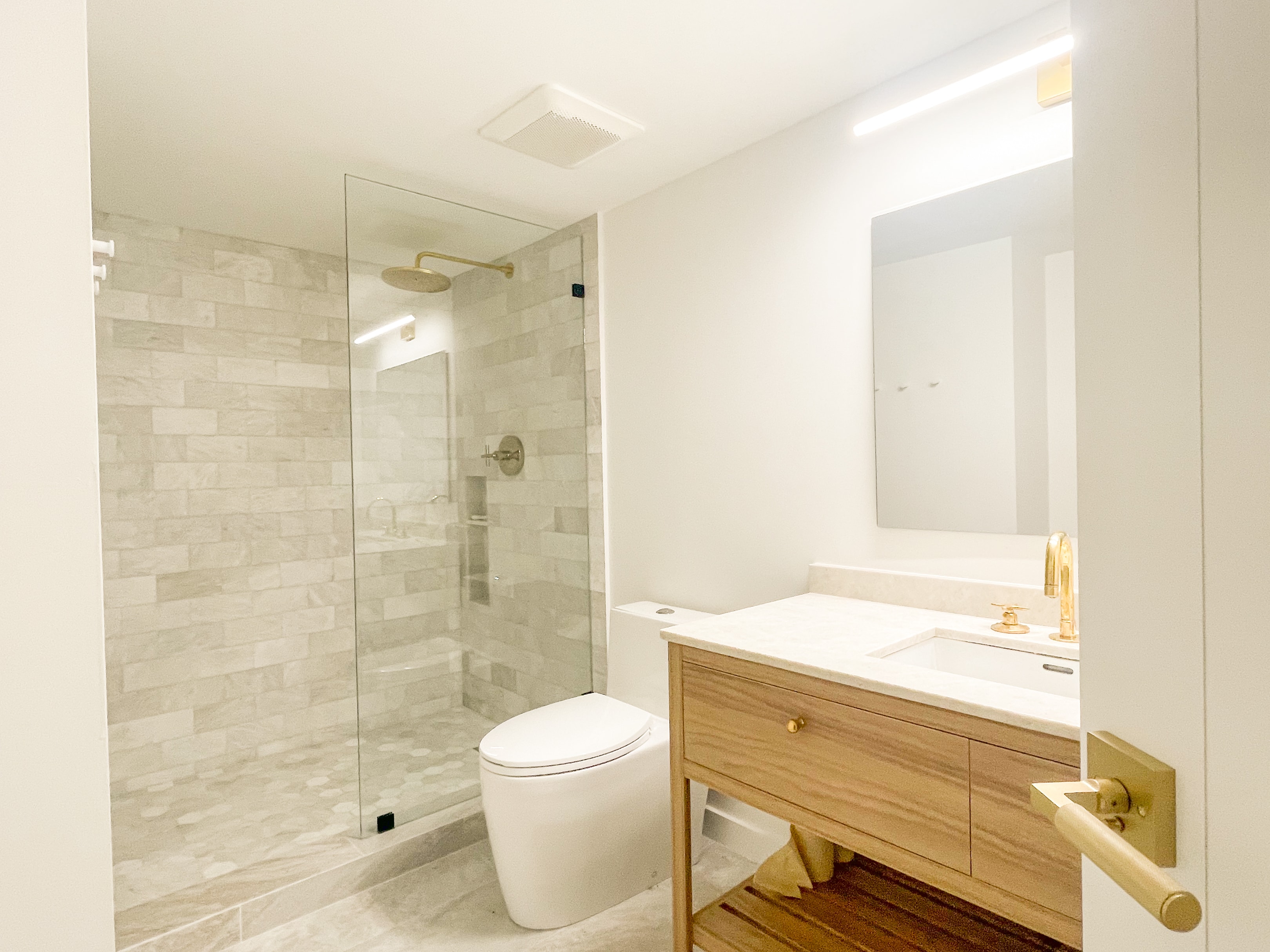 Bathroom vanity and glass-enclosed marble tile shower from entry angle