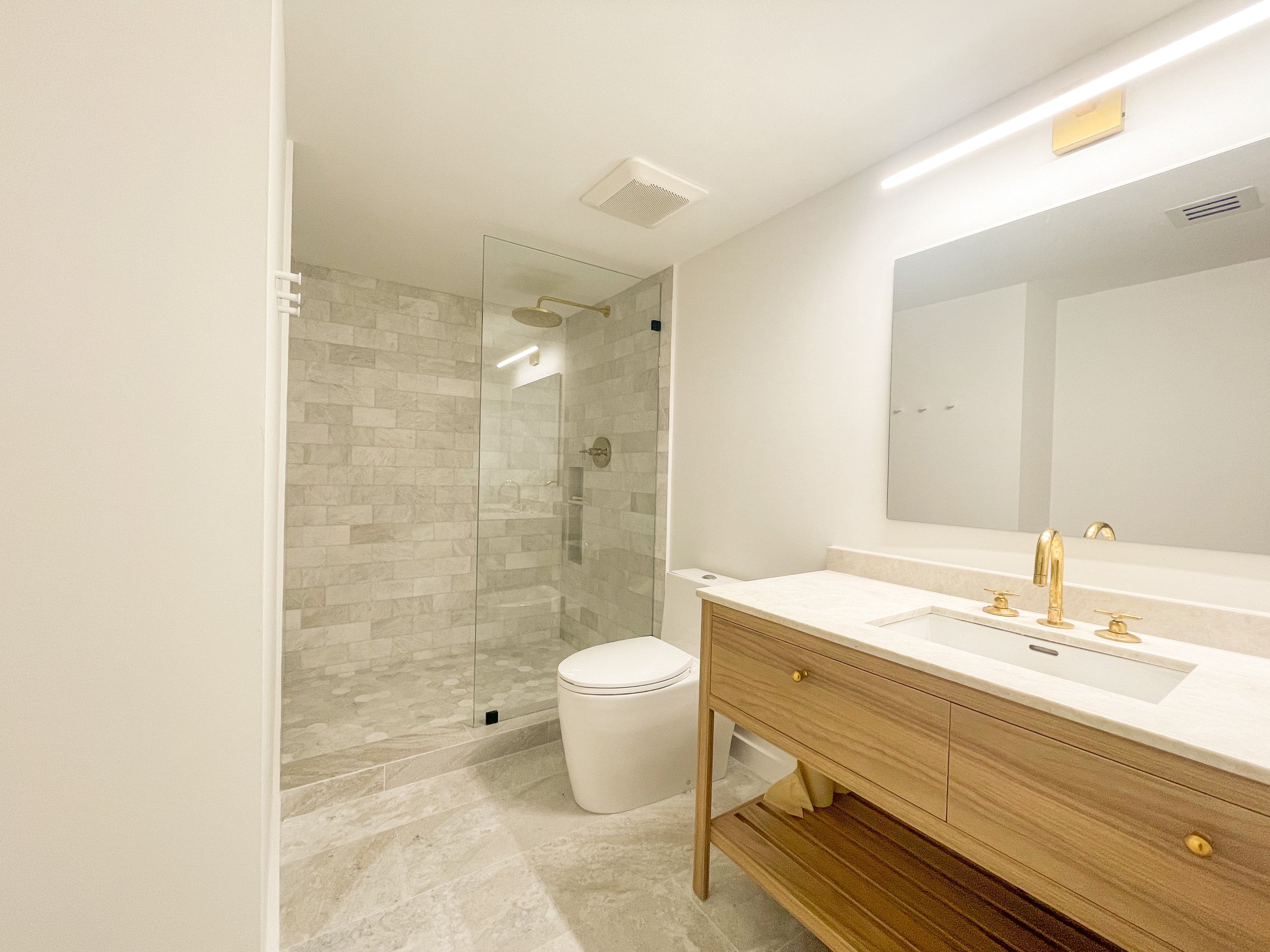 Bathroom with wood vanity, marble tile shower, and brass rain head
