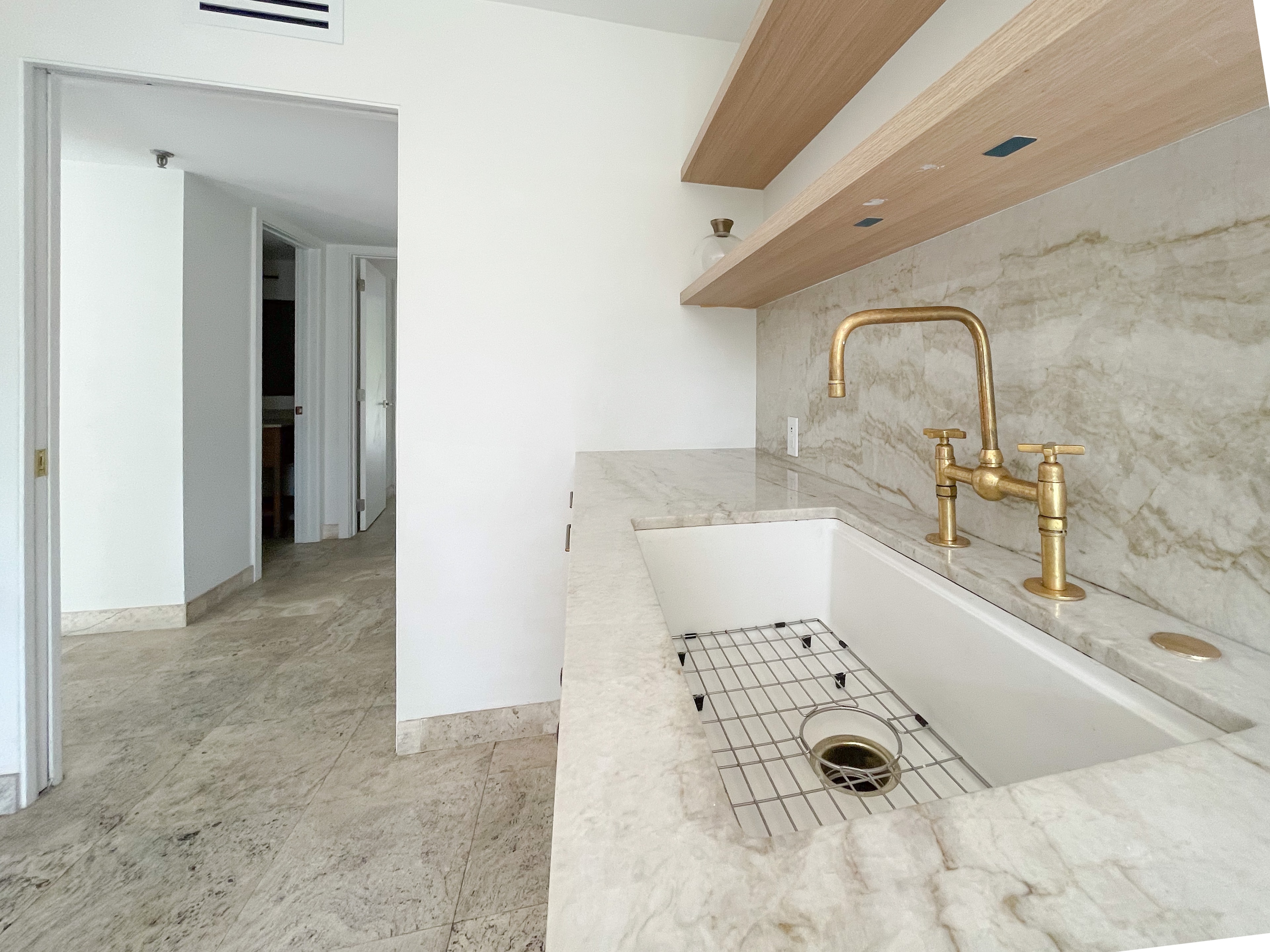Close-up of farmhouse sink with brass bridge faucet and marble slab backsplash