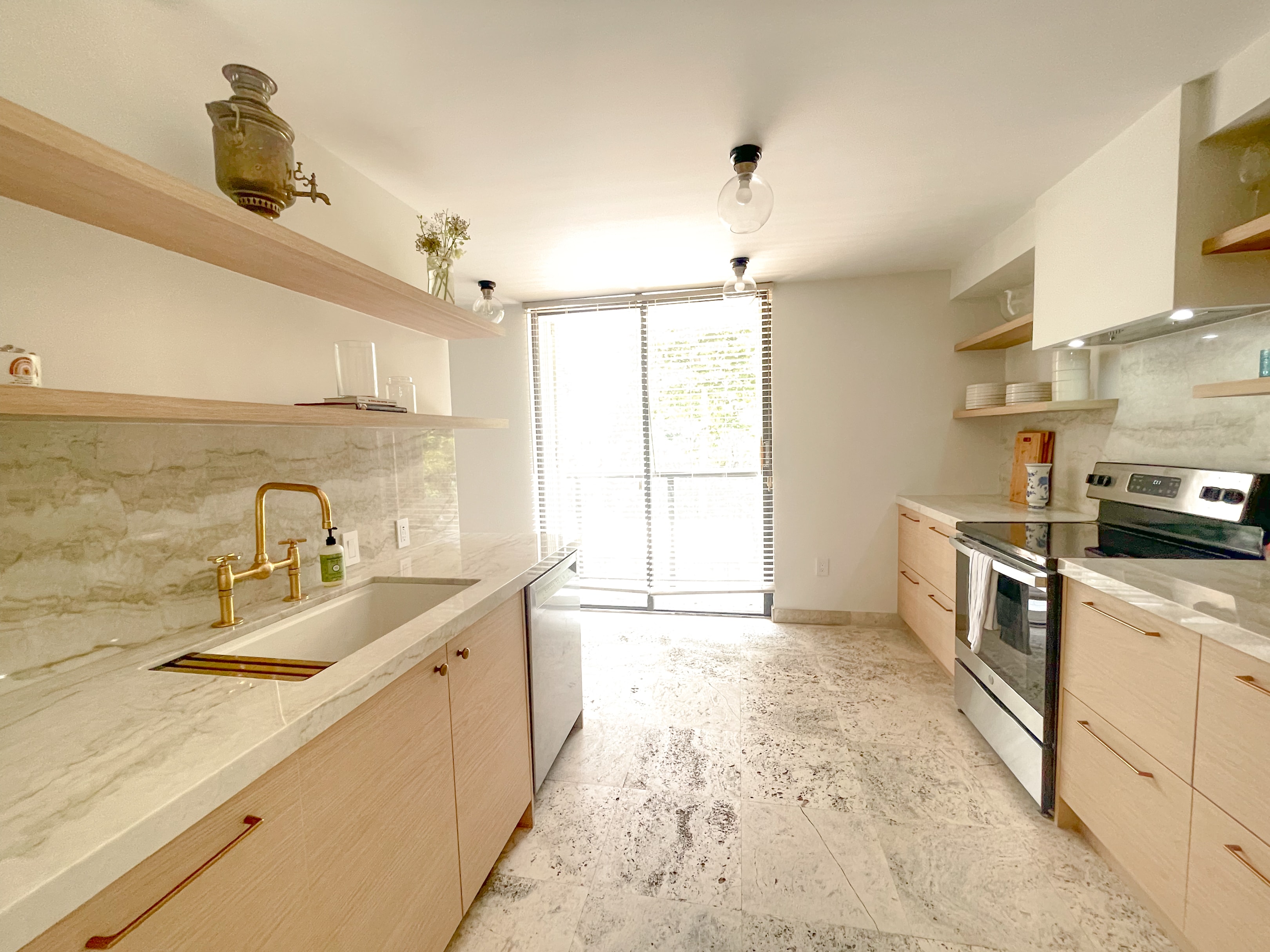 Galley kitchen with marble countertops, brass bridge faucet, and open wood shelving
