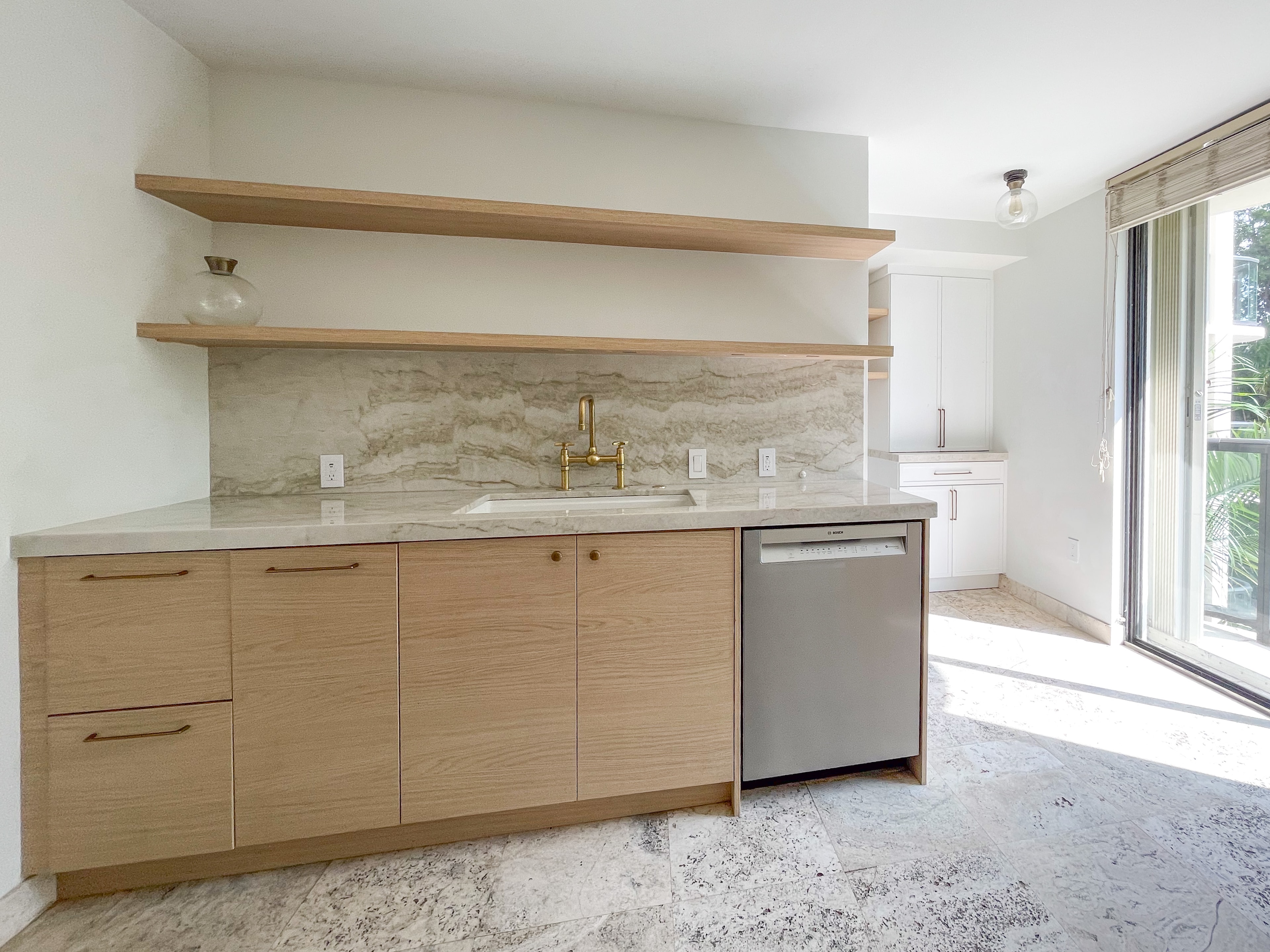 Full kitchen counter run with brass bridge faucet, marble backsplash, and Bosch dishwasher