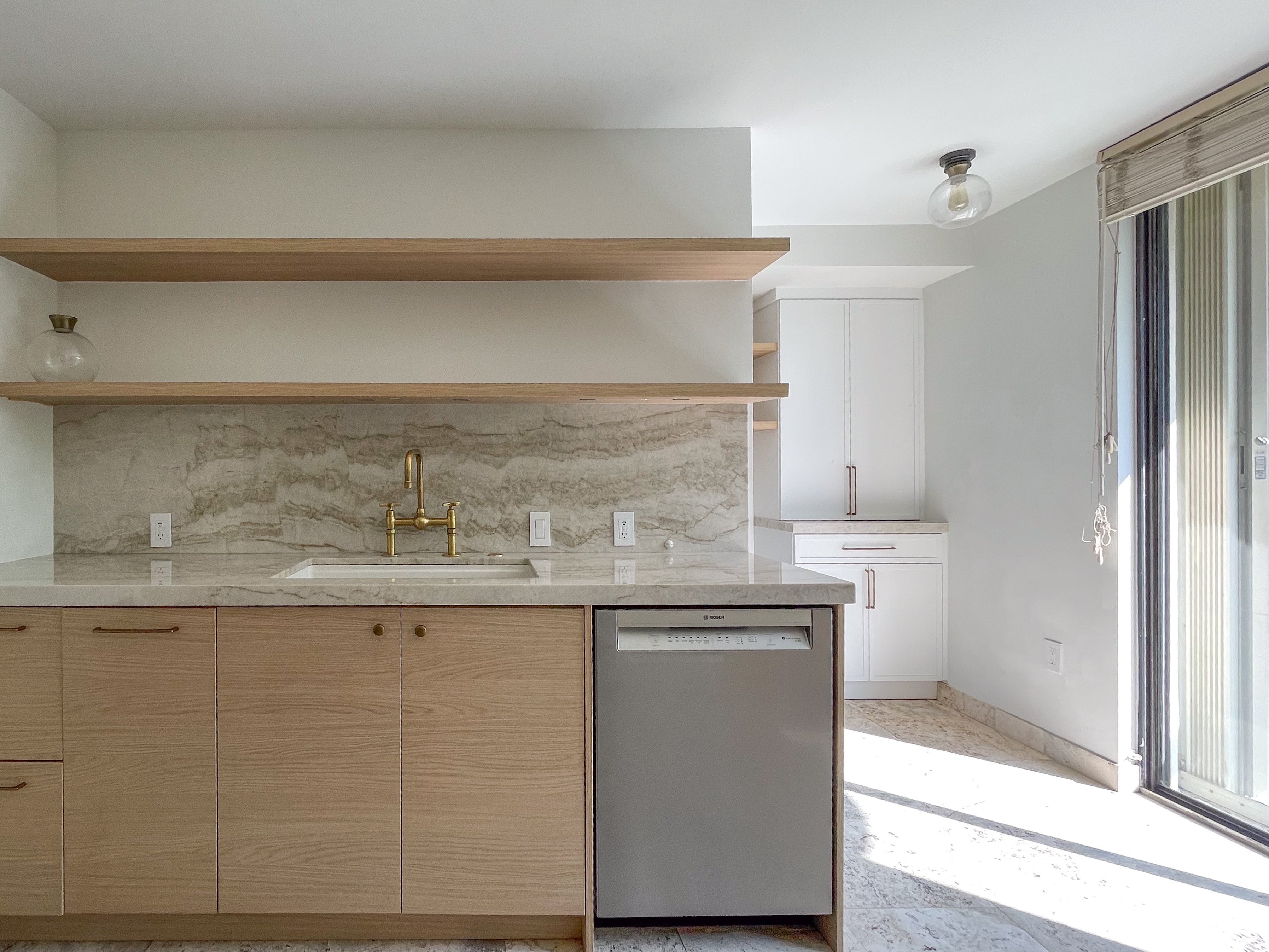 Kitchen sink counter with brass faucet and sliding glass door to terrace